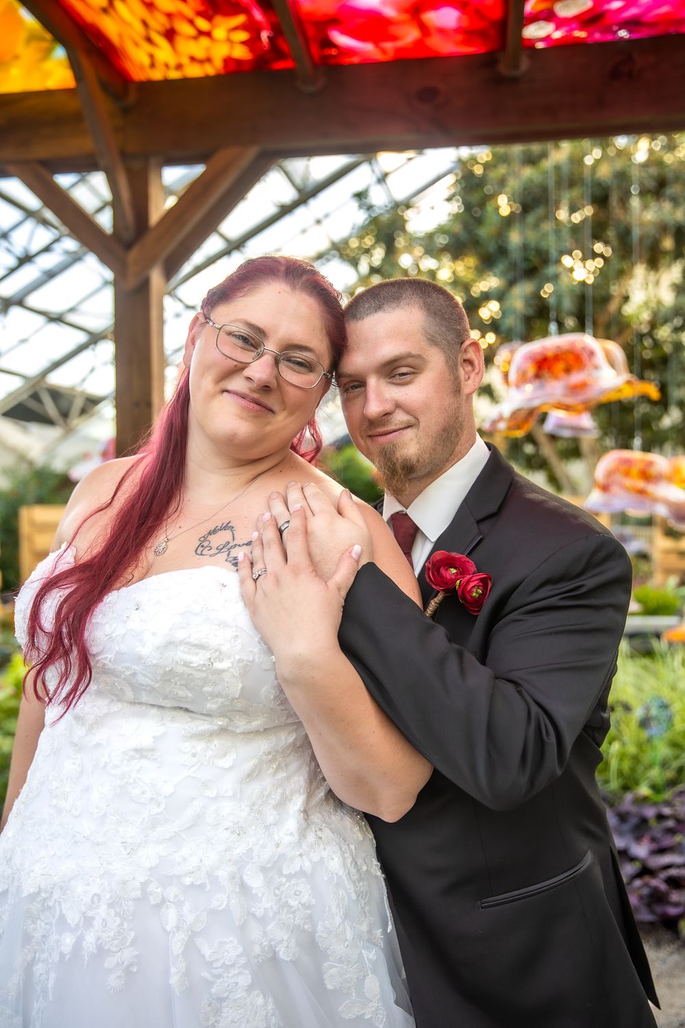 Cheerful newlyweds pose together under a floral garden pergola during an outdoor wedding celebration.