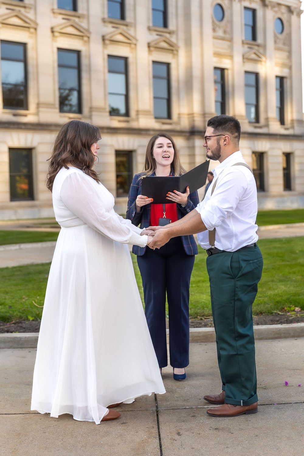 Wedding ceremony taking place outside historic building with officiant and couple in formal attire.