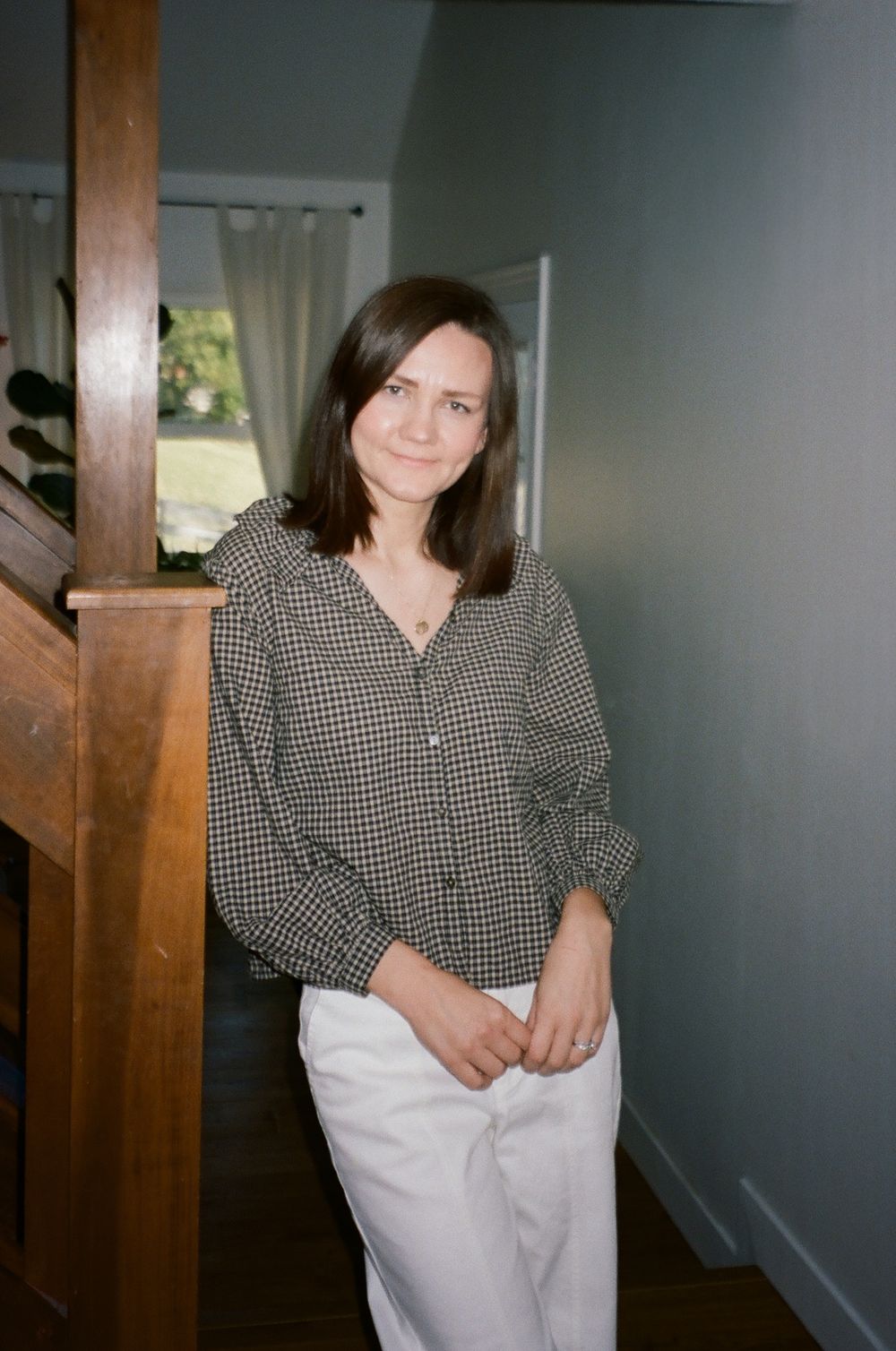 A person in black clothing poses against an orange wall in a minimalist studio setting.