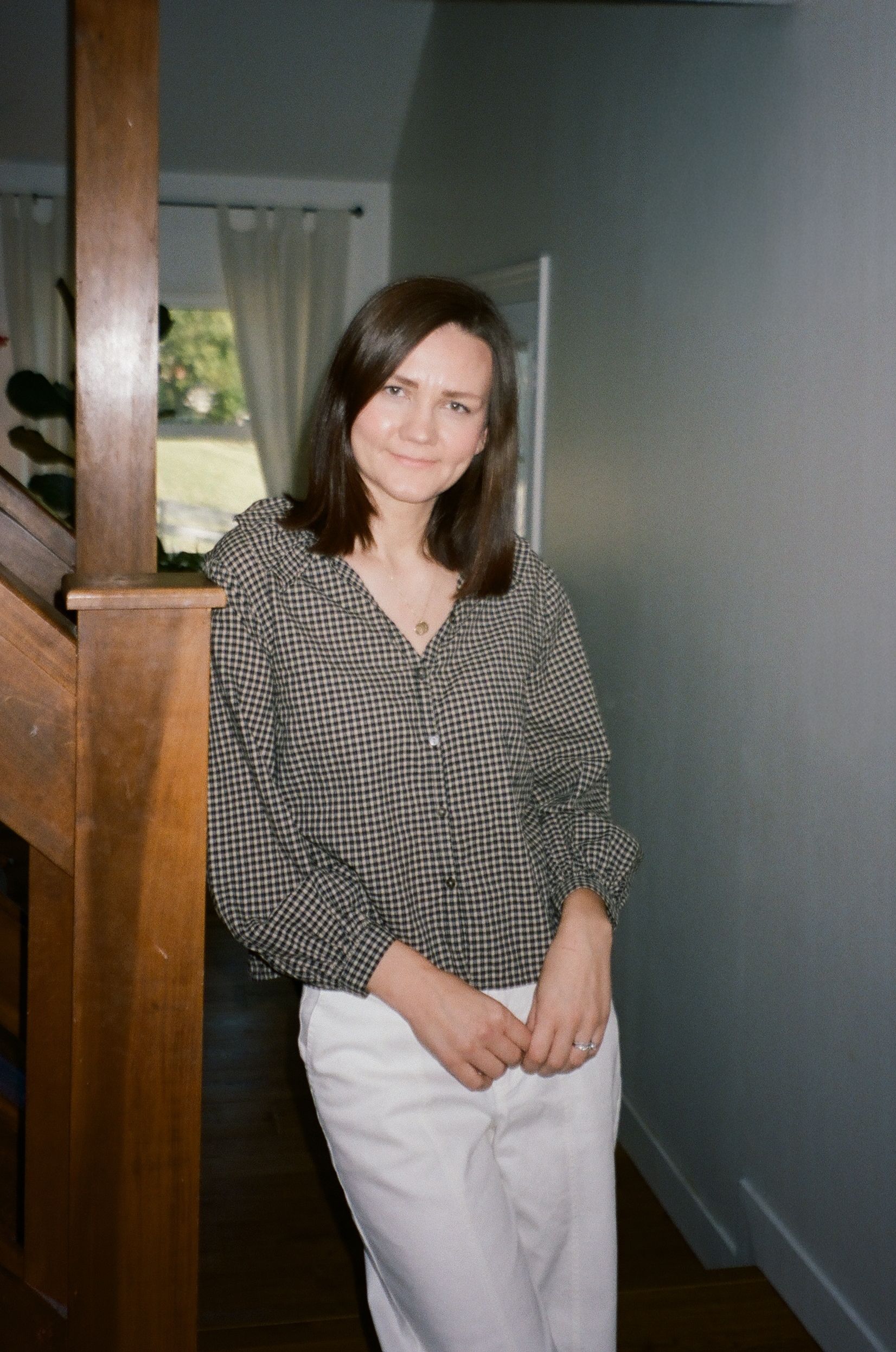 A person in black clothing poses against an orange wall in a minimalist studio setting.