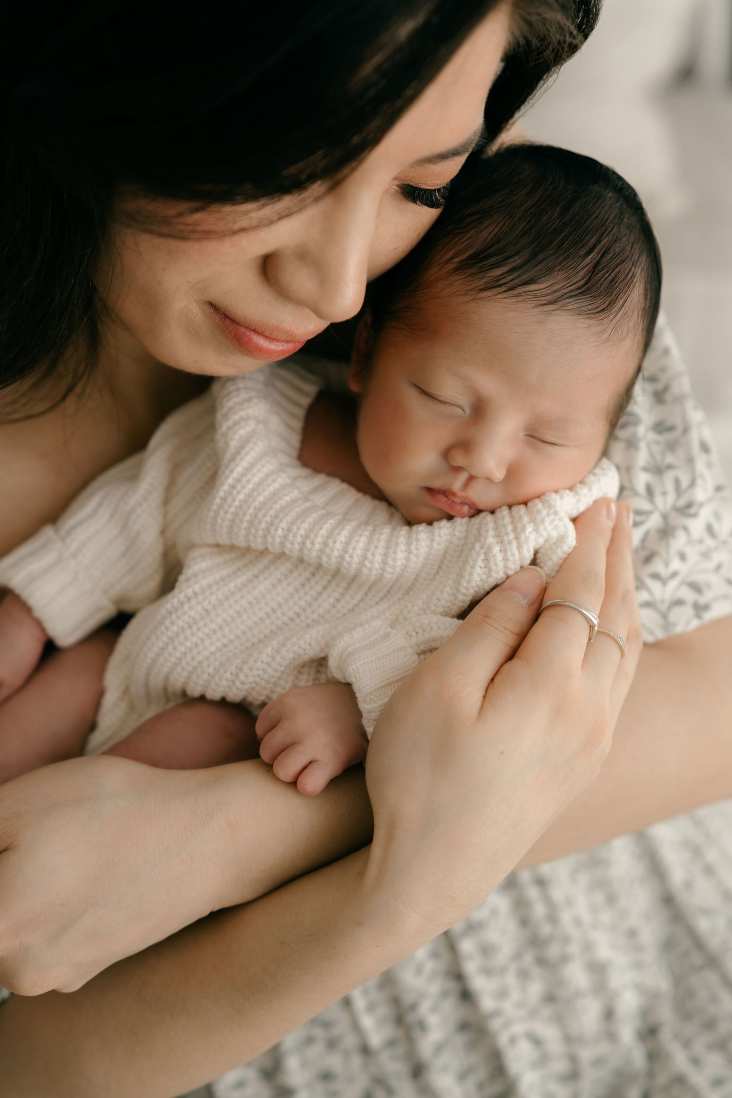 Tender moment between mother and sleeping newborn baby both wearing white knit sweaters.