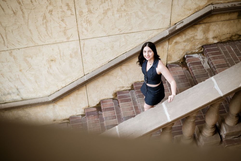 A woman in a navy dress descending vintage stone stairs in dramatic lighting.