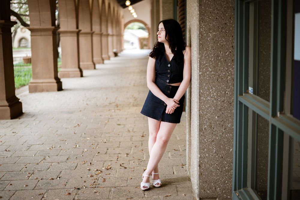 Young couple in a formal dress and suit stand together in a brick archway corridor.