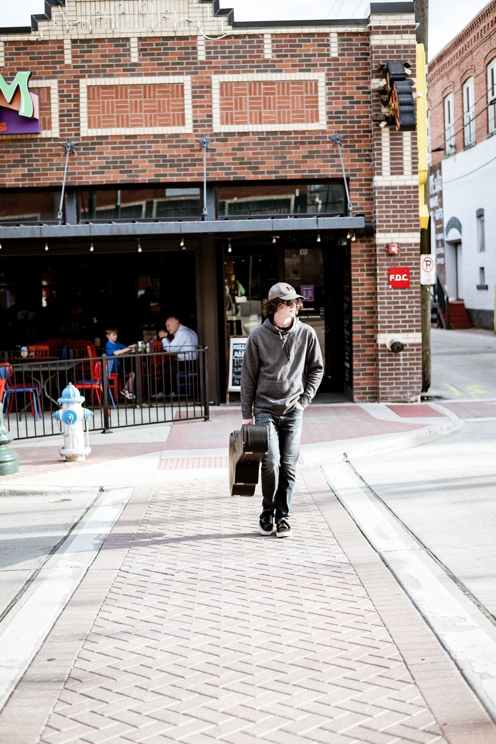 Person walking on city sidewalk carrying bag outside brick building storefront.