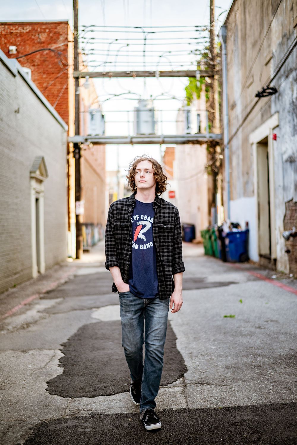 Person wearing plaid shirt and jeans standing in urban alley against painted walls.