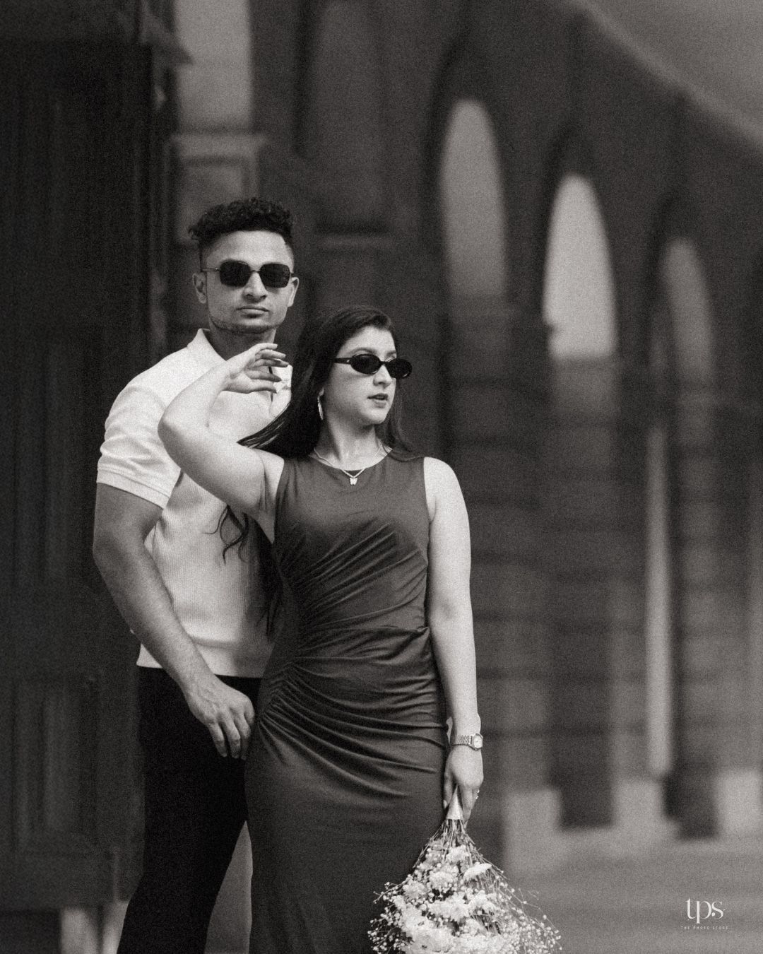 Stylish couple in sunglasses posing together on an urban street in black and white.