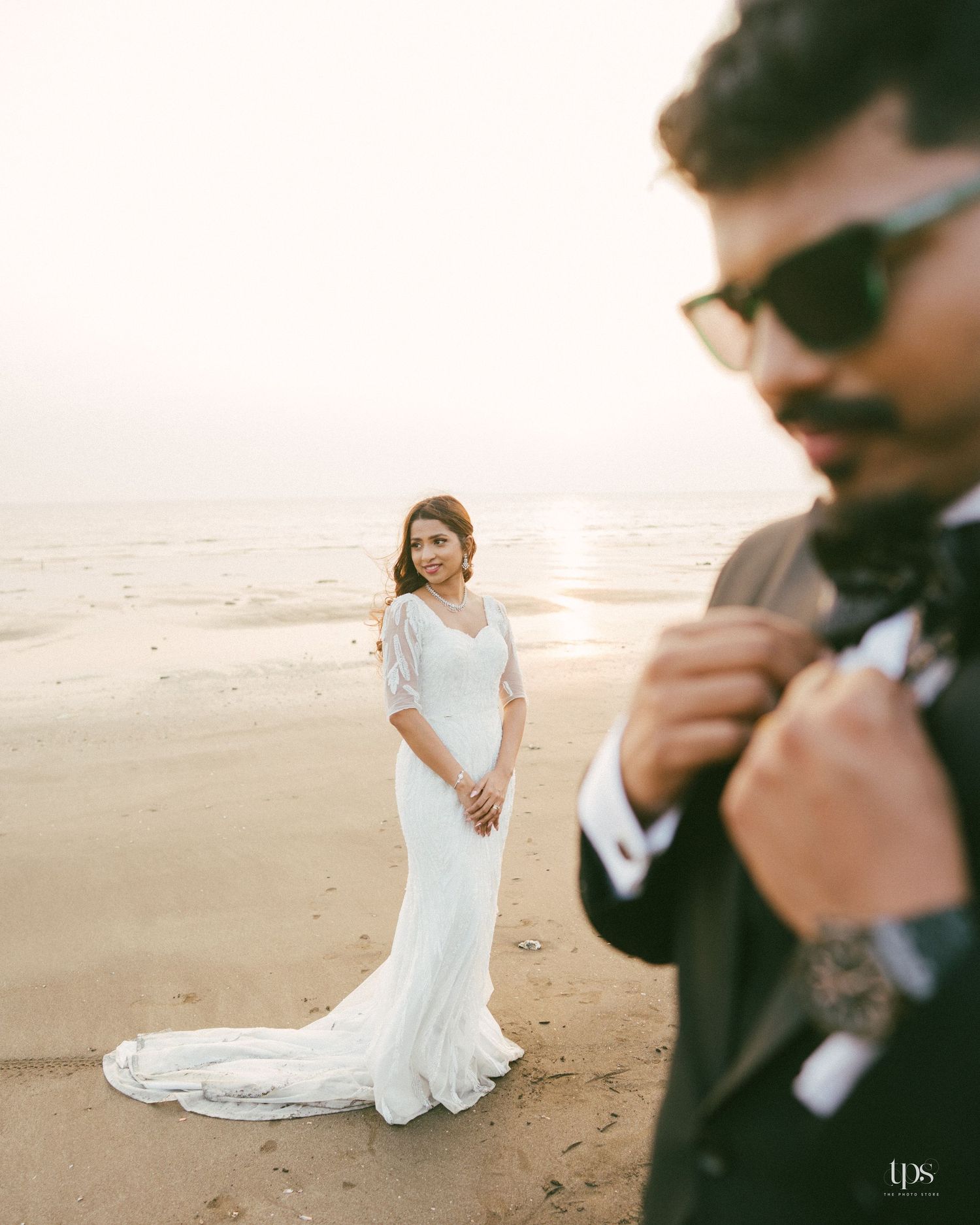 A bride poses in an elegant white gown on a beach at sunset.