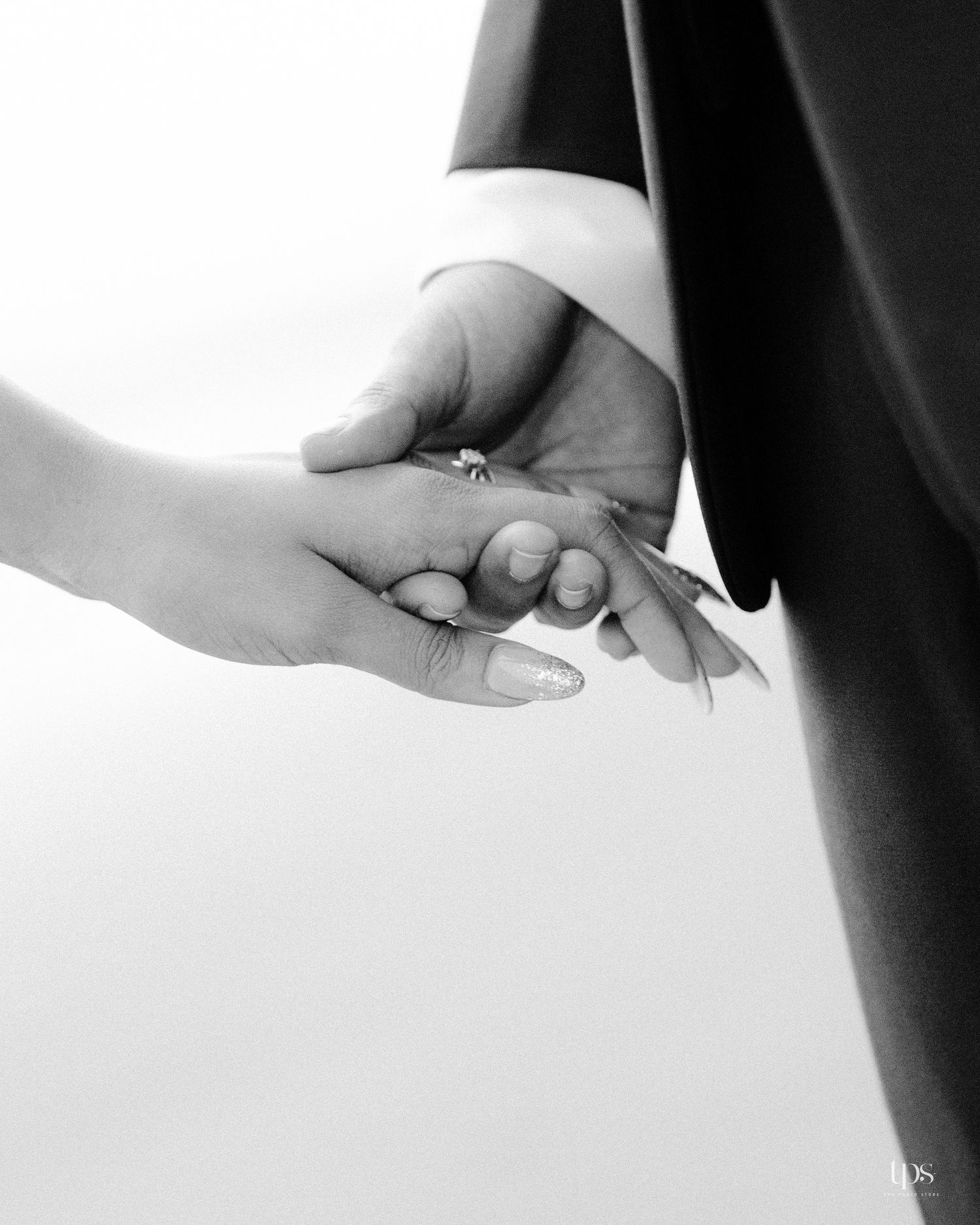 A black and white close-up of hands holding with an engagement ring.