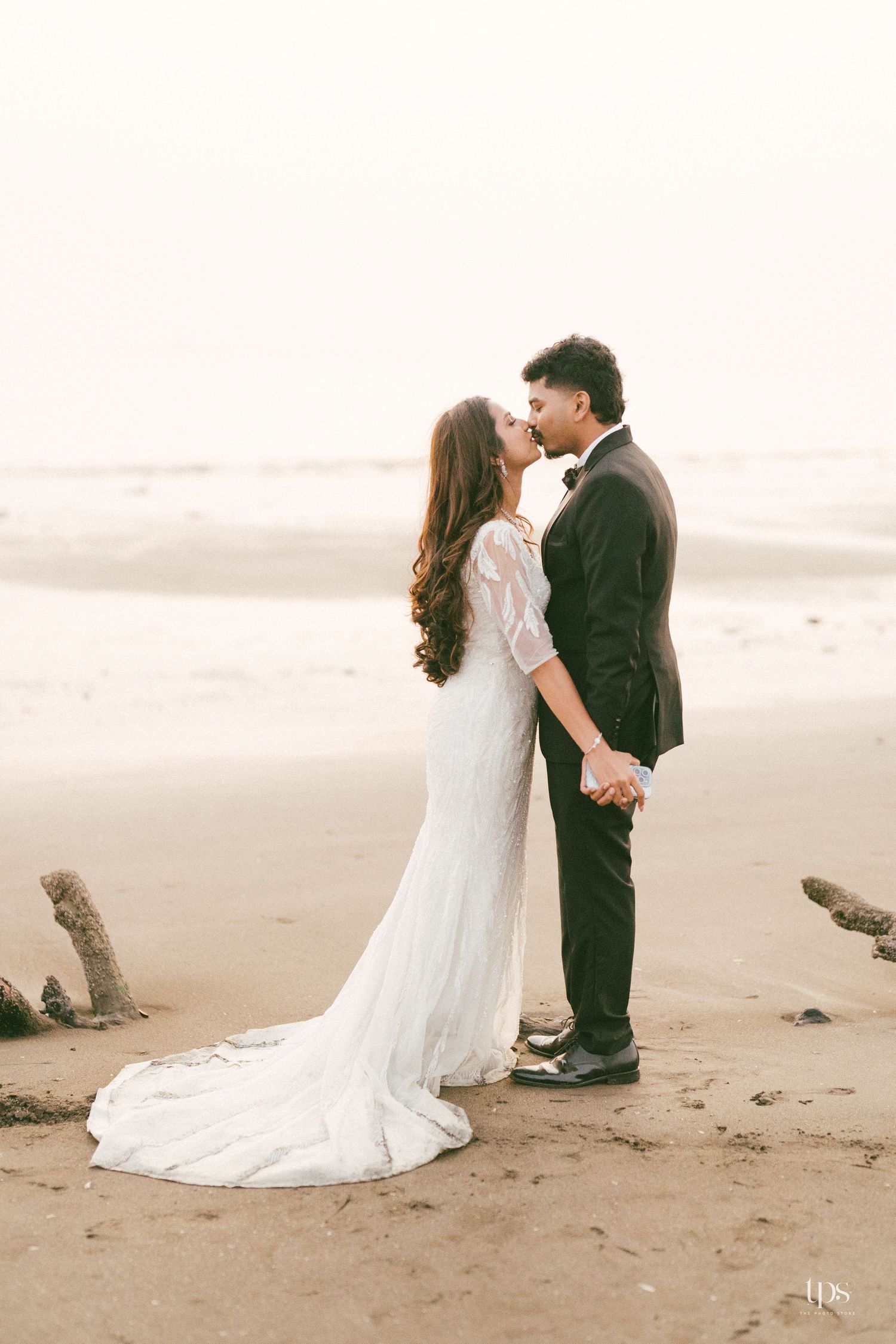 A romantic wedding portrait on a beach with waves in the background.