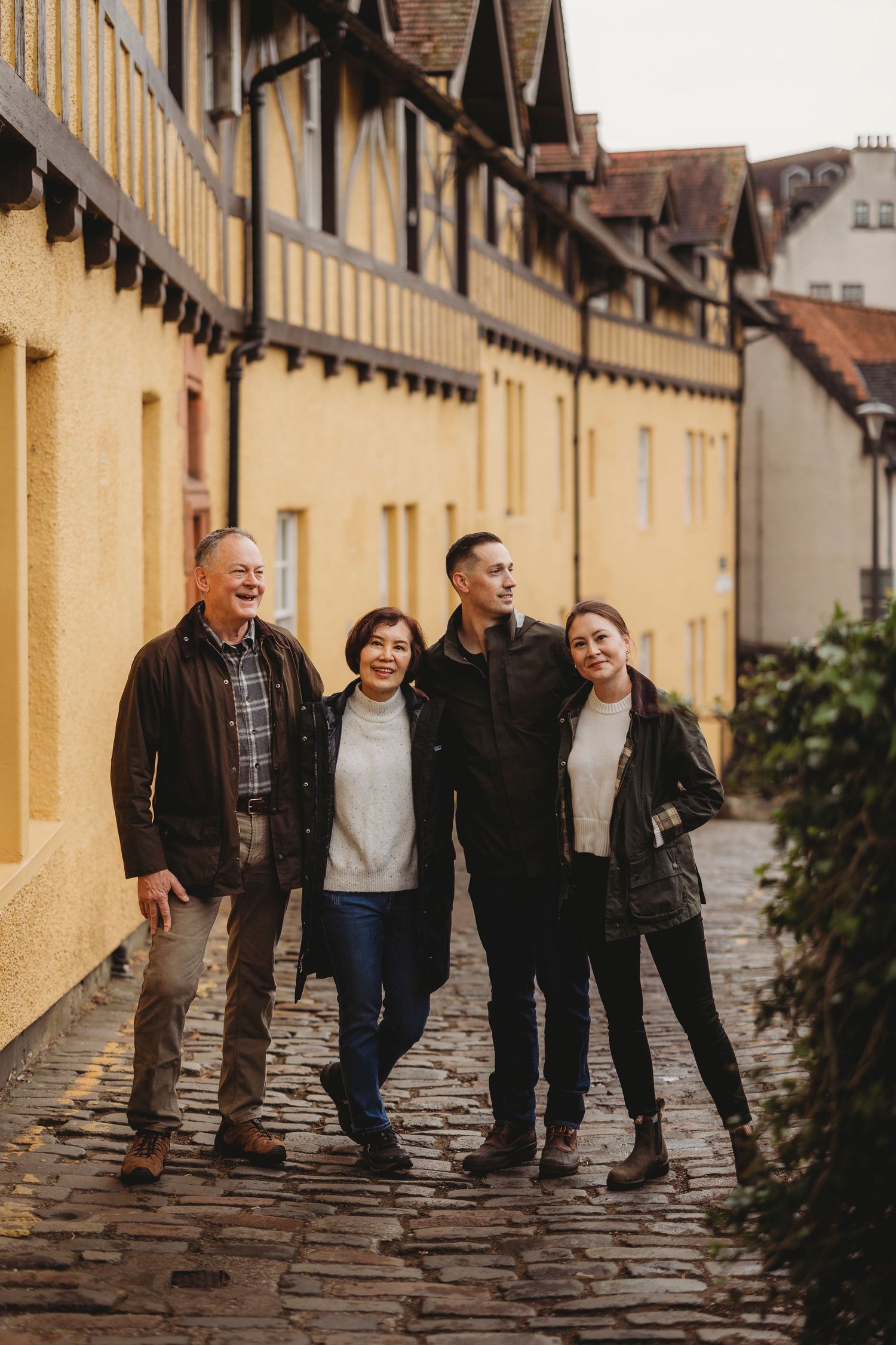 A group walks together along a charming cobblestone path beside yellow buildings in an old European neighborhood.