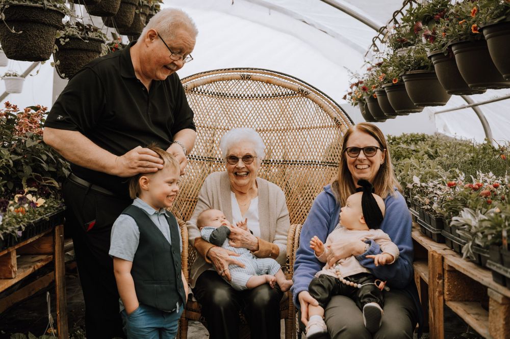 Multi-generational family gathering in a greenhouse with a woven peacock chair and hanging plants.