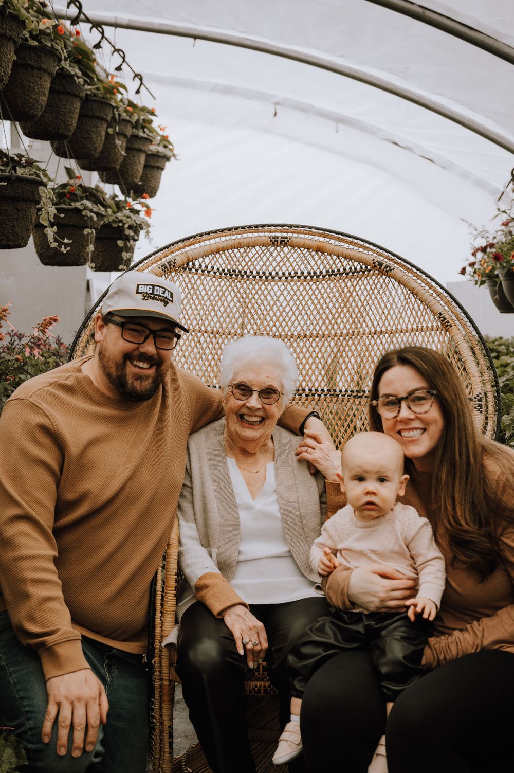 Family portrait in a greenhouse with a decorative woven chair and hanging planters.