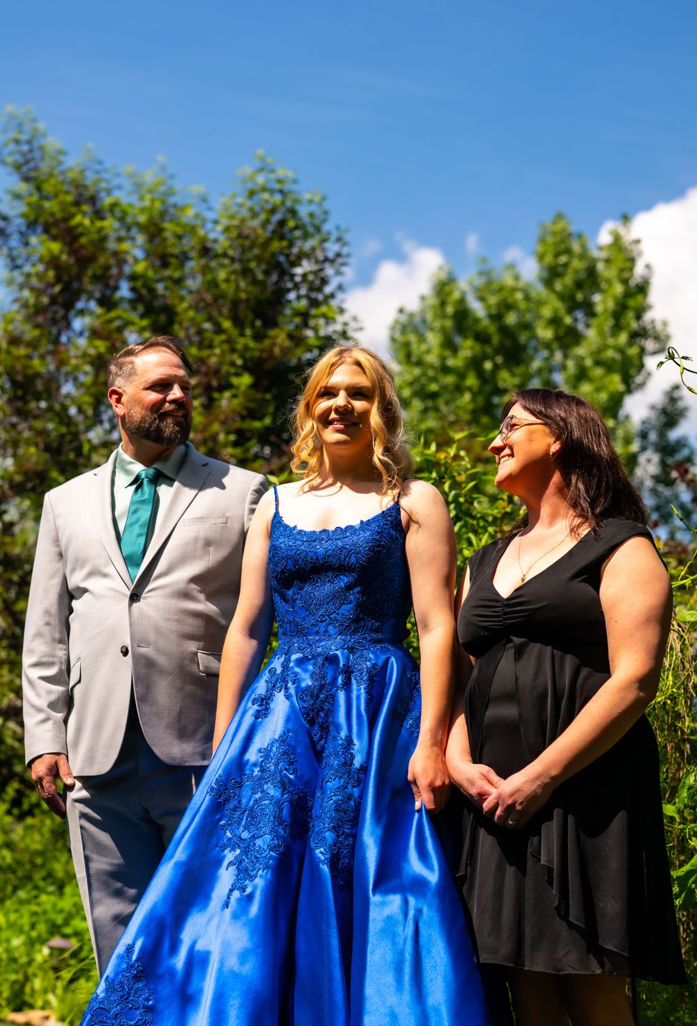 Outdoor formal portrait with three people against lush summer greenery.