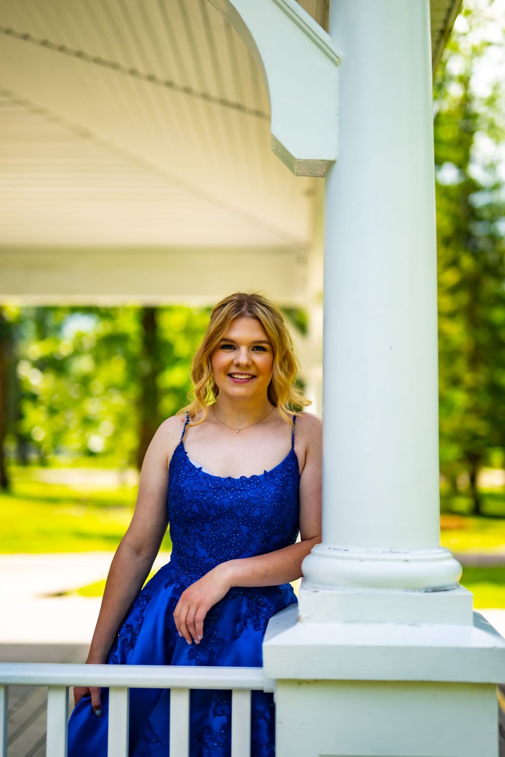 Elegant blue formal dress captured on white porch with natural backdrop.