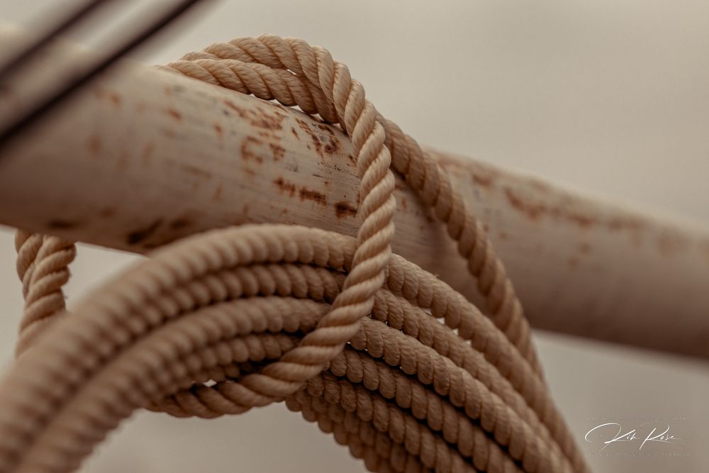 Close-up of a thick twisted rope tied around a rusty metal pole, showcasing nautical knot detail.