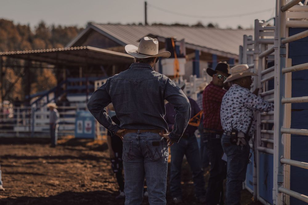 Two cowboys standing near metal rodeo chutes watching the arena at an outdoor rodeo event.