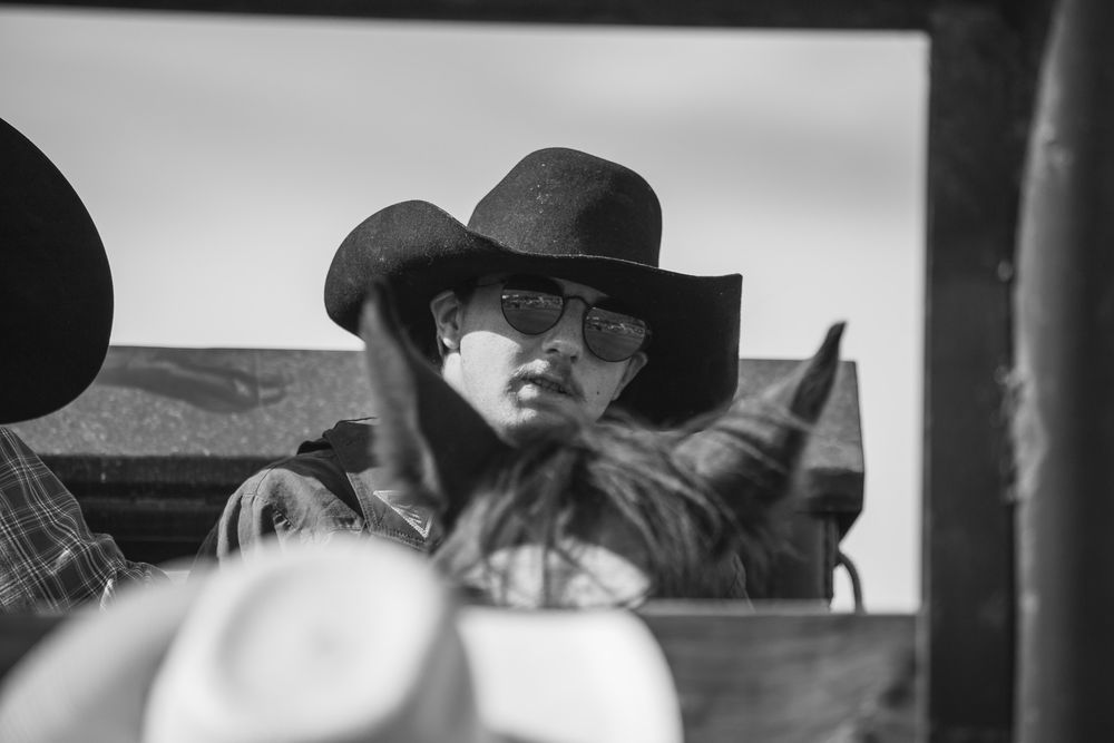 Black and white portrait of woman in cowboy hat and sunglasses at rodeo.