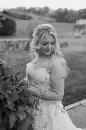 Black and white portrait of a bride in a lace wedding dress standing by vines in a garden setting.