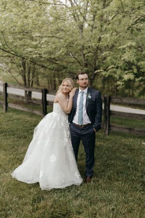 A couple poses together on their wedding day in front of a tree-lined path.