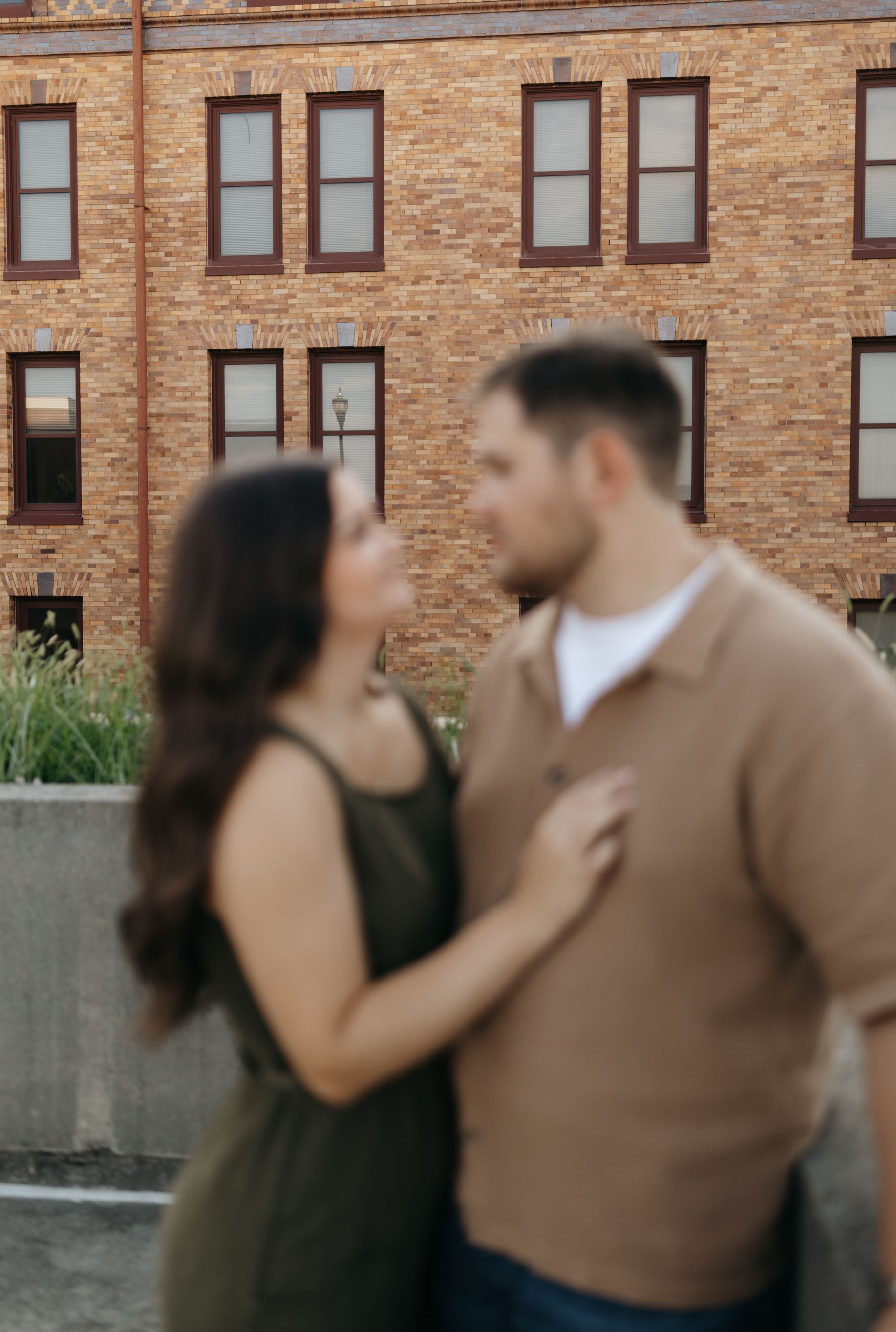 A couple sharing an intimate moment against a rustic brick building facade.