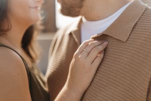 Close-up of a hand with an engagement ring resting on a tan sweater.