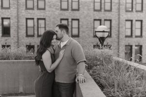 A couple embracing against a backdrop of classic brick architecture in black and white.