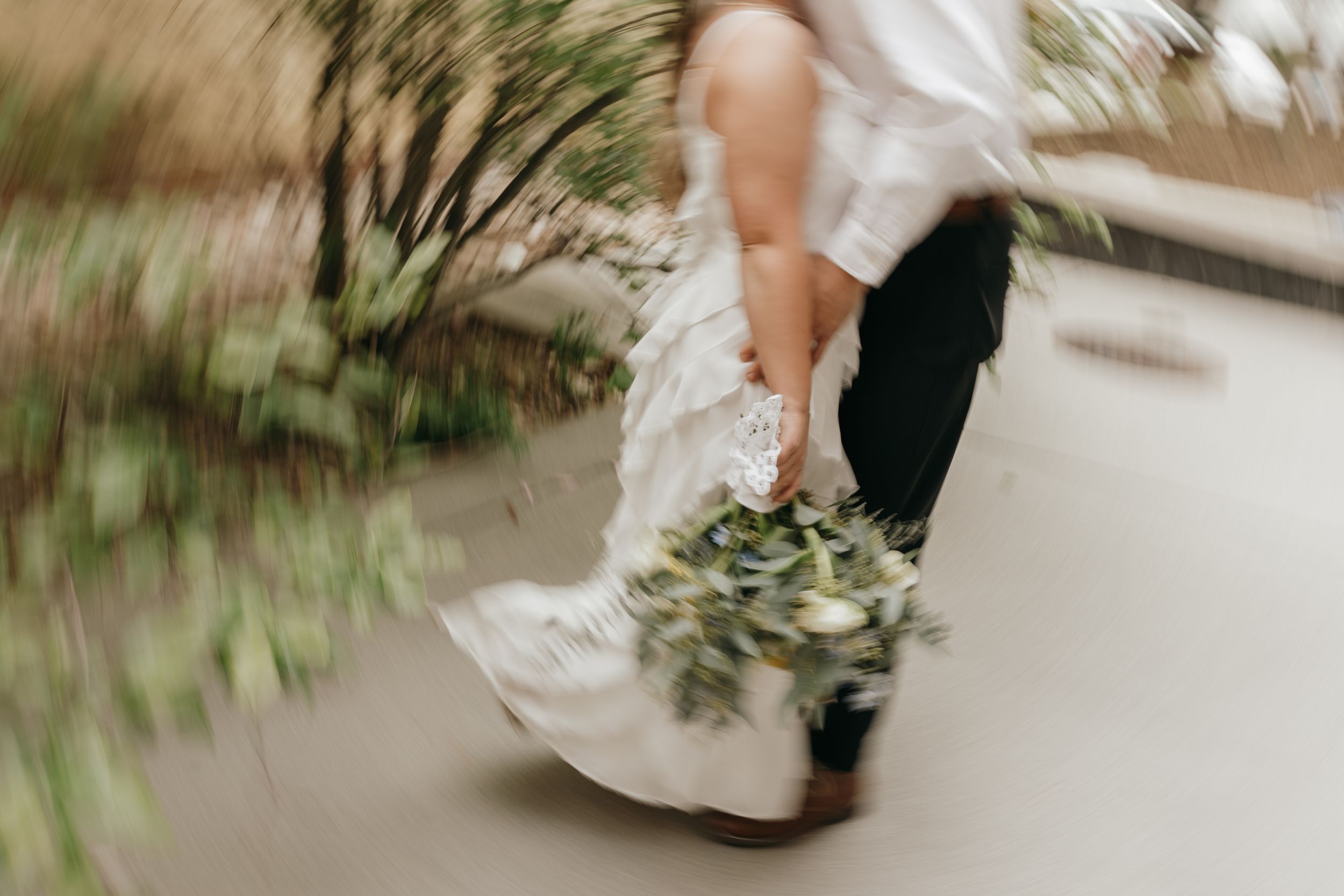 Close-up shot of a bride's dress and bouquet in motion while walking.