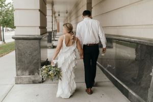 Newlyweds walking together down a columned hallway with the bride carrying a floral bouquet.