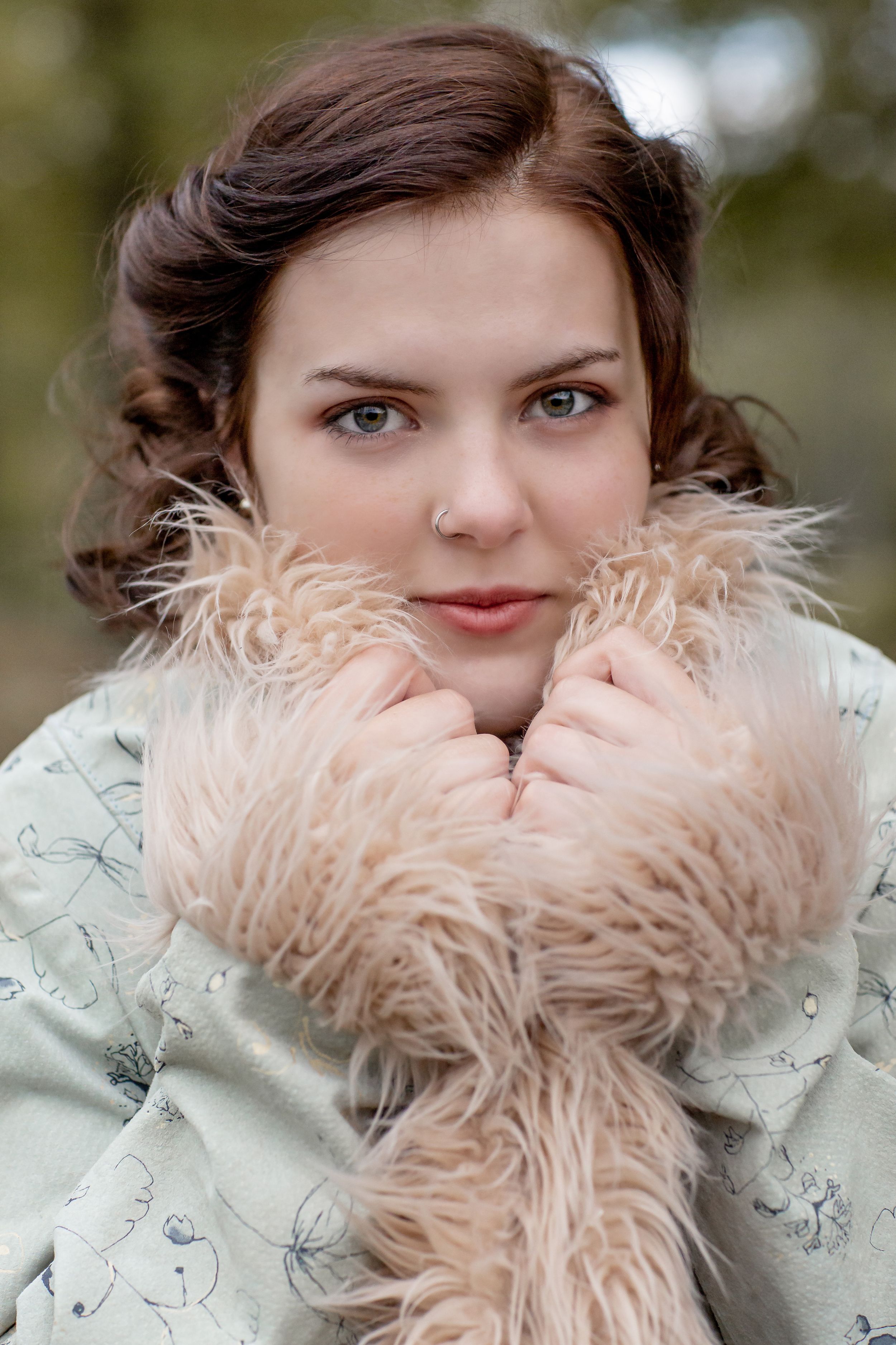 Young brunette woman in floral coat holding a fluffy fur collar close to her face outdoors.