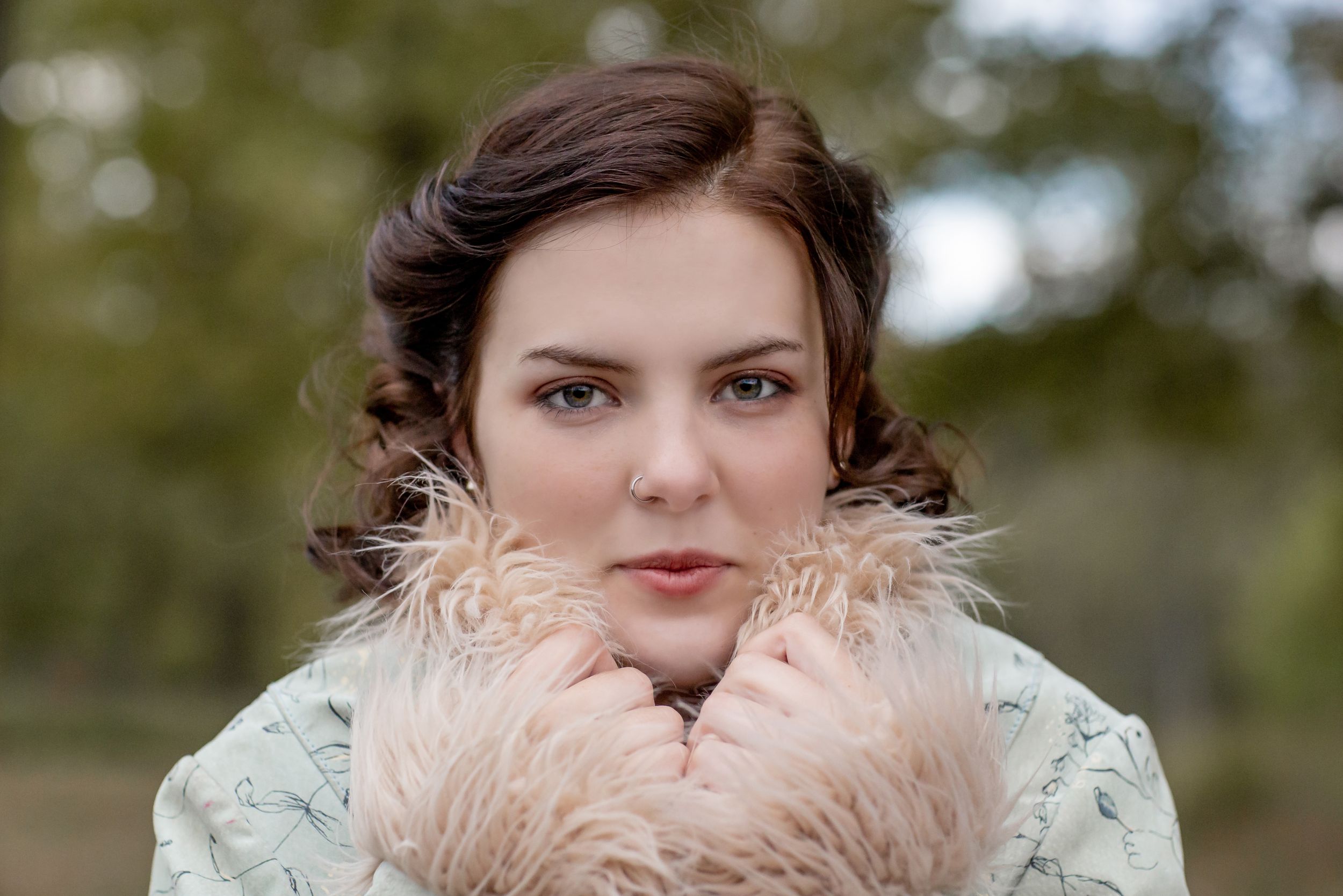 Young woman in vintage style holding fluffy pink collar coat outdoors in park.
