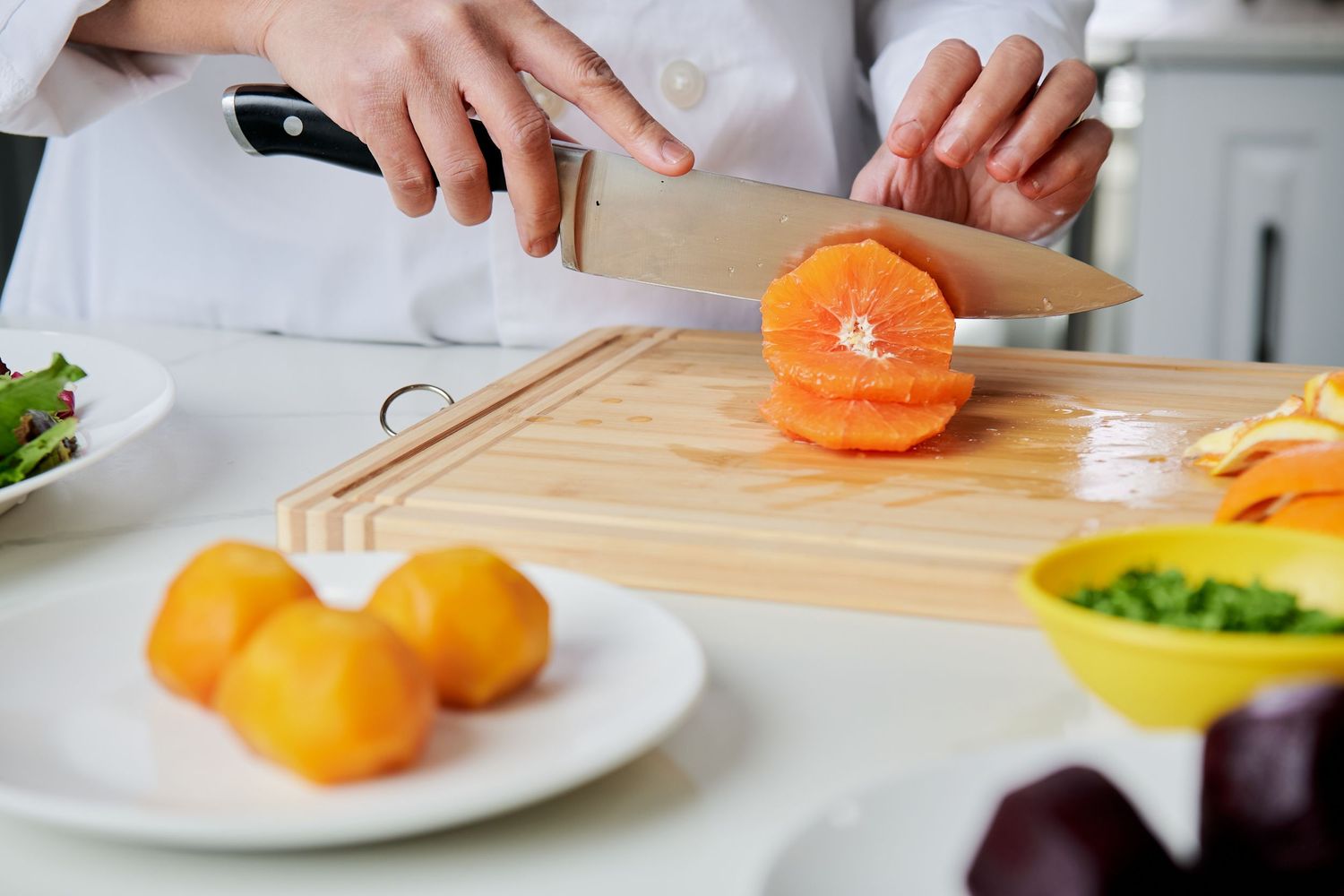 Fresh mandarin oranges being sliced on a wooden cutting board in a bright kitchen setting.