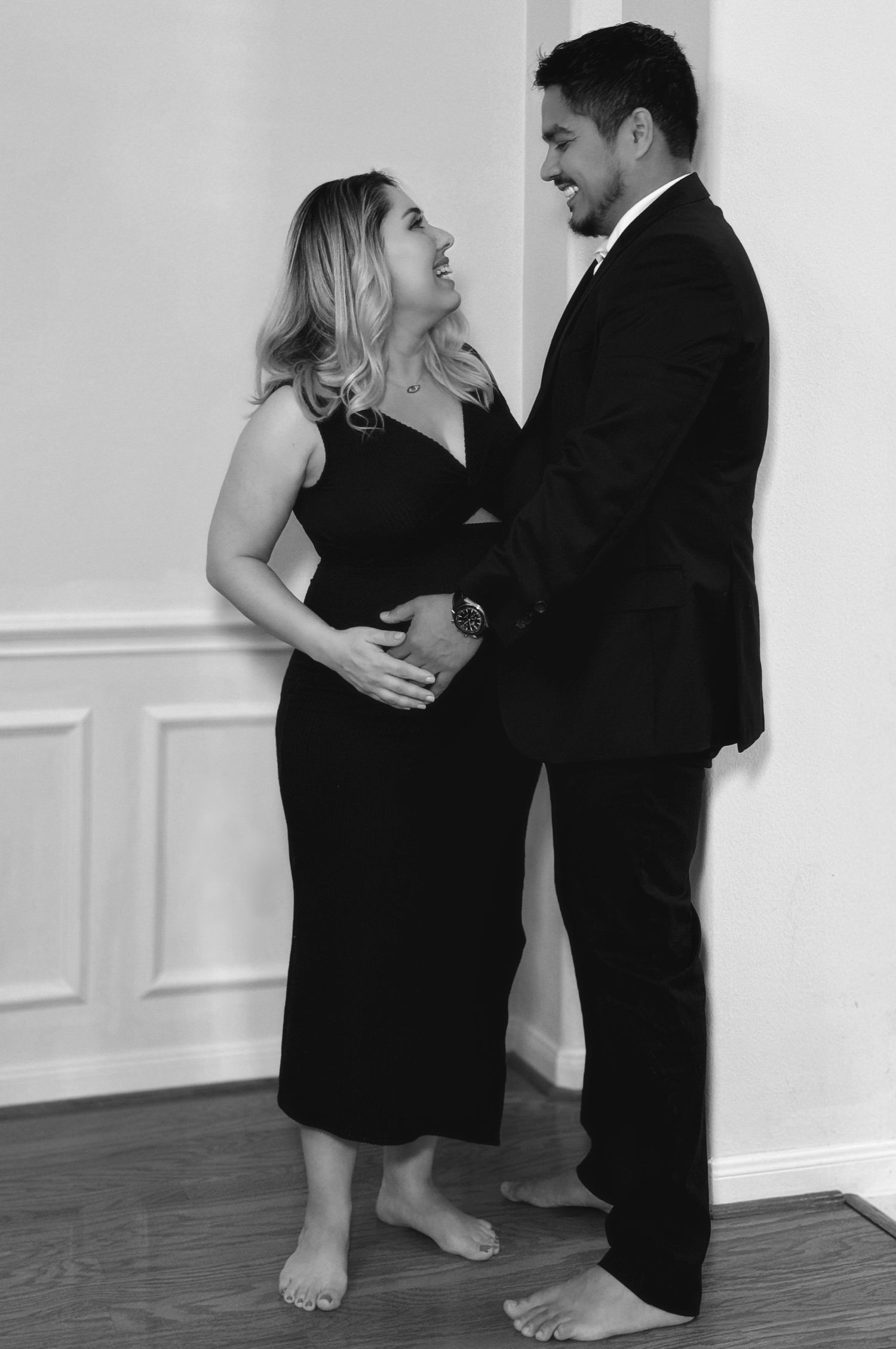 A couple shares an intimate moment in black and white photography against a white wall.