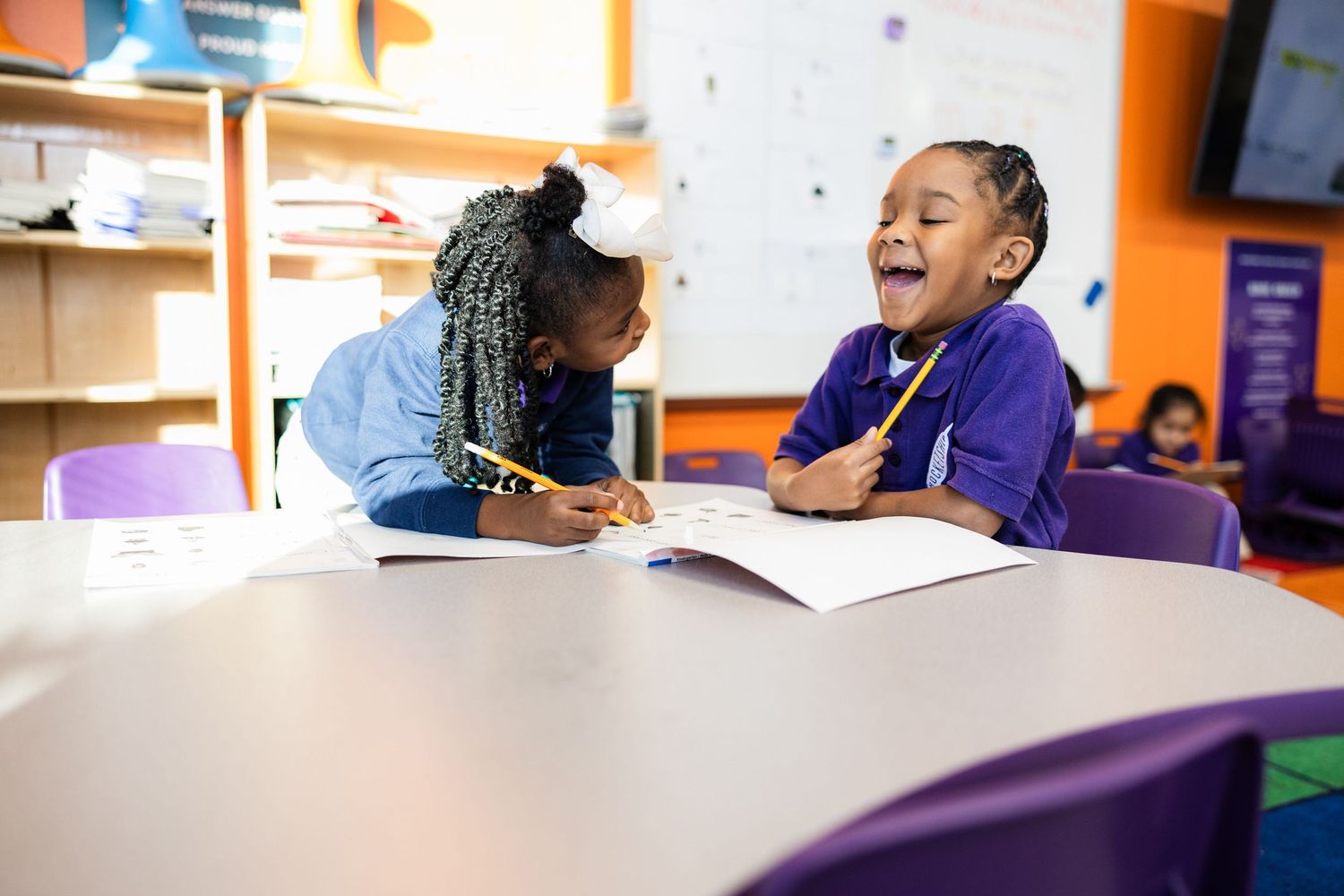 Children engaged in collaborative learning activities at colorful classroom tables.