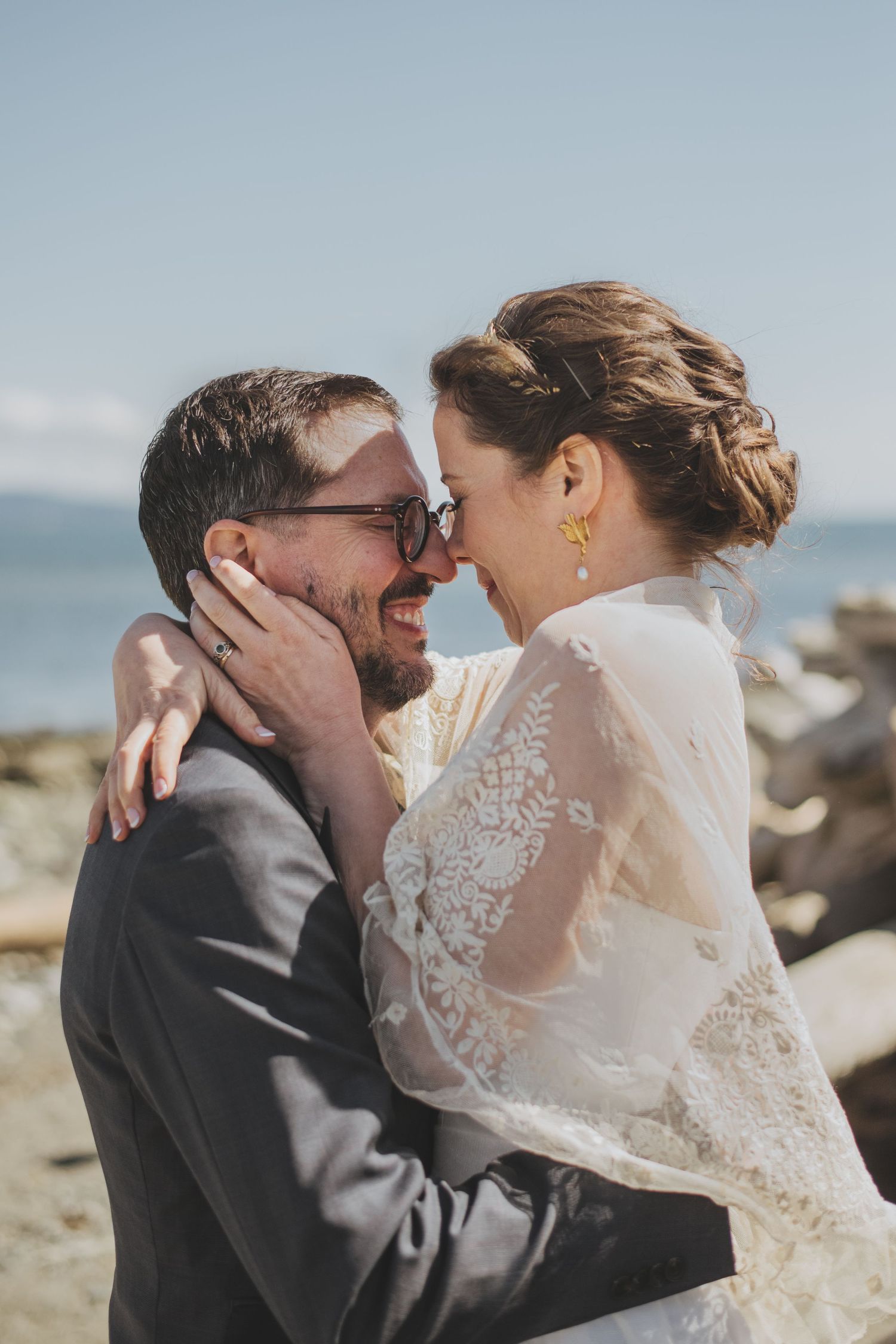 An intimate wedding moment captured on a rocky beach with bright natural lighting.