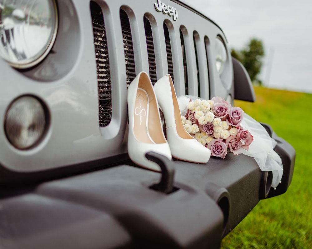 White bridal heels and rose bouquet resting on vintage Jeep grill.