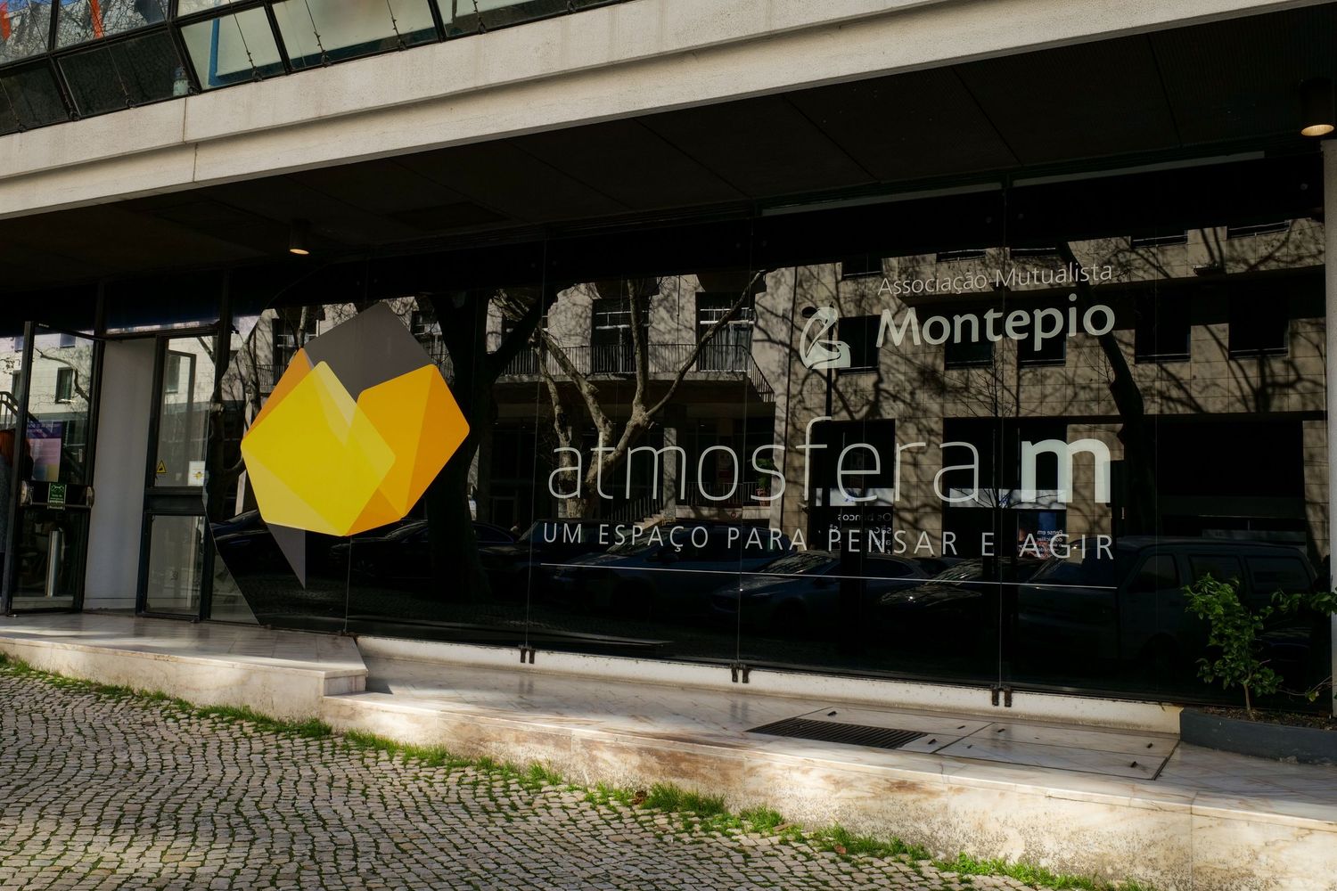 Montepio Atmosfera.m modern building exterior with reflective glass facade and cobblestone sidewalk.