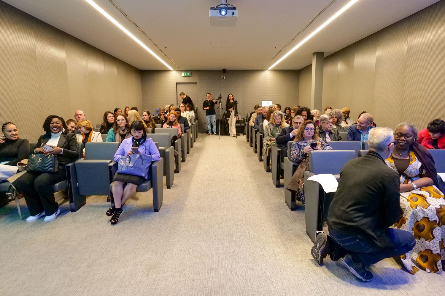Diverse audience seated in modern conference room during professional business event presentation.