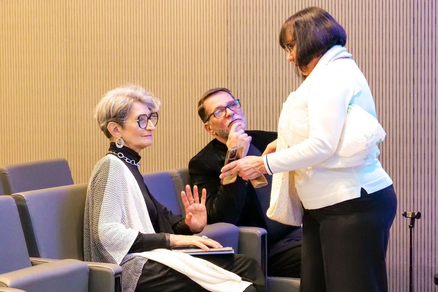 Three professionals engaged in conversation during a business conference networking session.