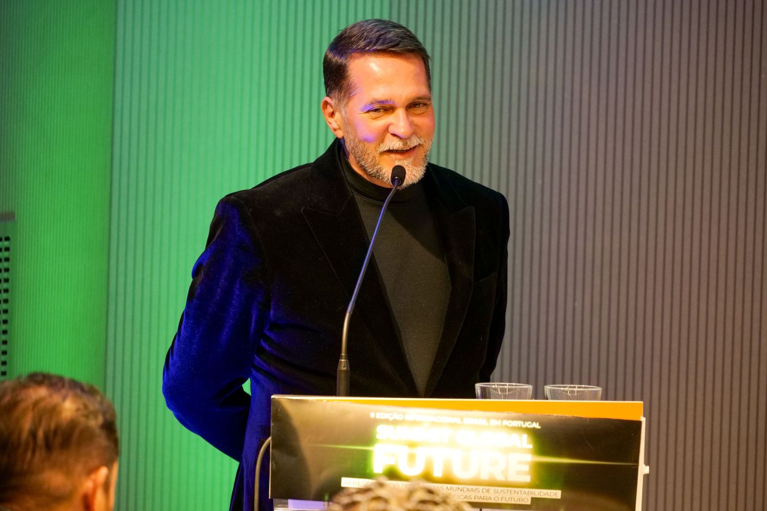 Confident man in black suit speaks at a podium during a formal corporate event.