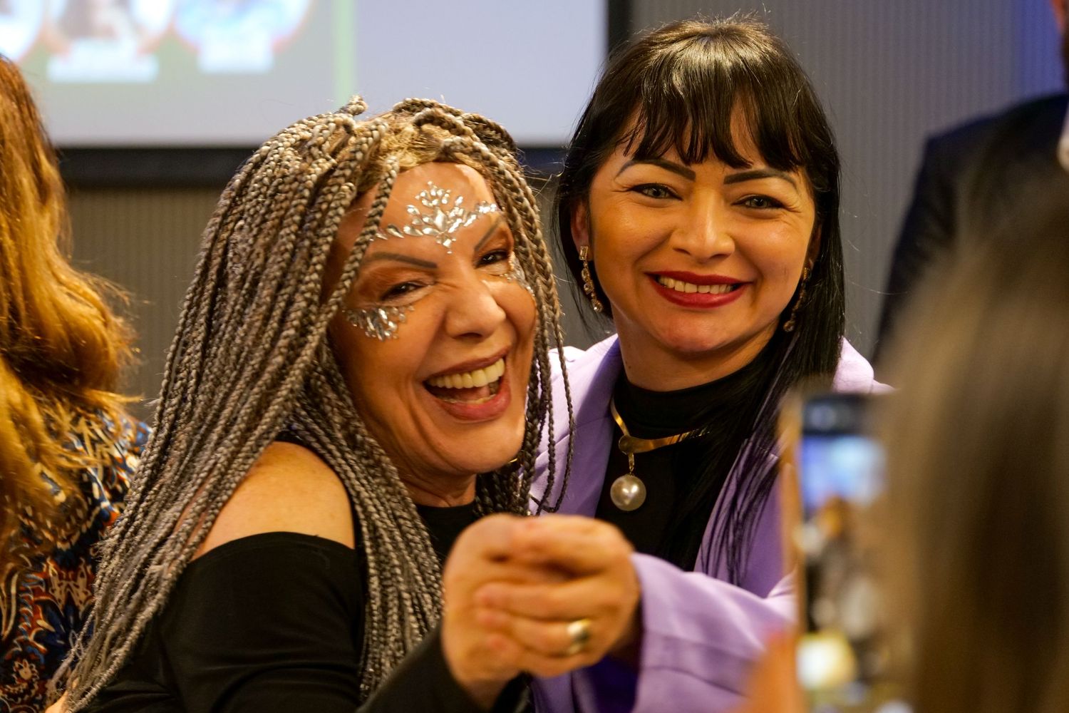 Two smiling women pose for a selfie at a festive networking event.