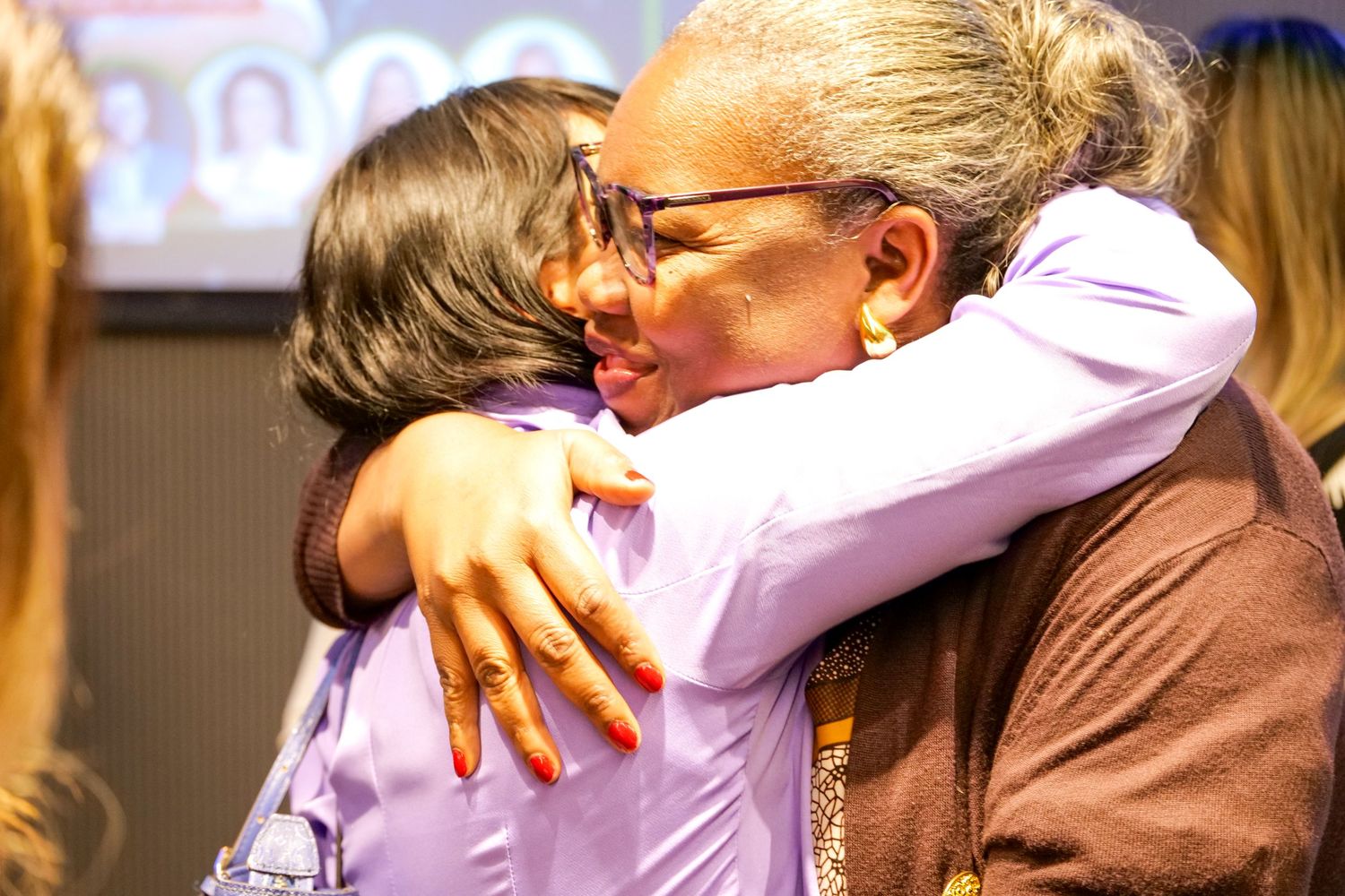 Two women share a warm embrace at an emotional professional conference event.