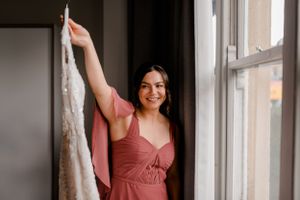 Person holding up white lace wedding dress by window in natural light.