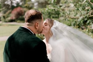 A romantic wedding kiss captured in a garden setting with the bride's veil flowing in the breeze.