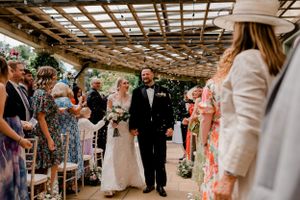 Wedding ceremony processional under a wooden pergola with natural light streaming through.