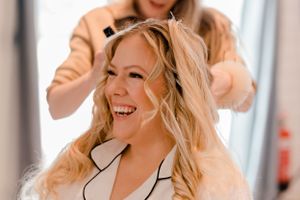 A joyful moment captured during bridal preparations with blonde hair being styled.