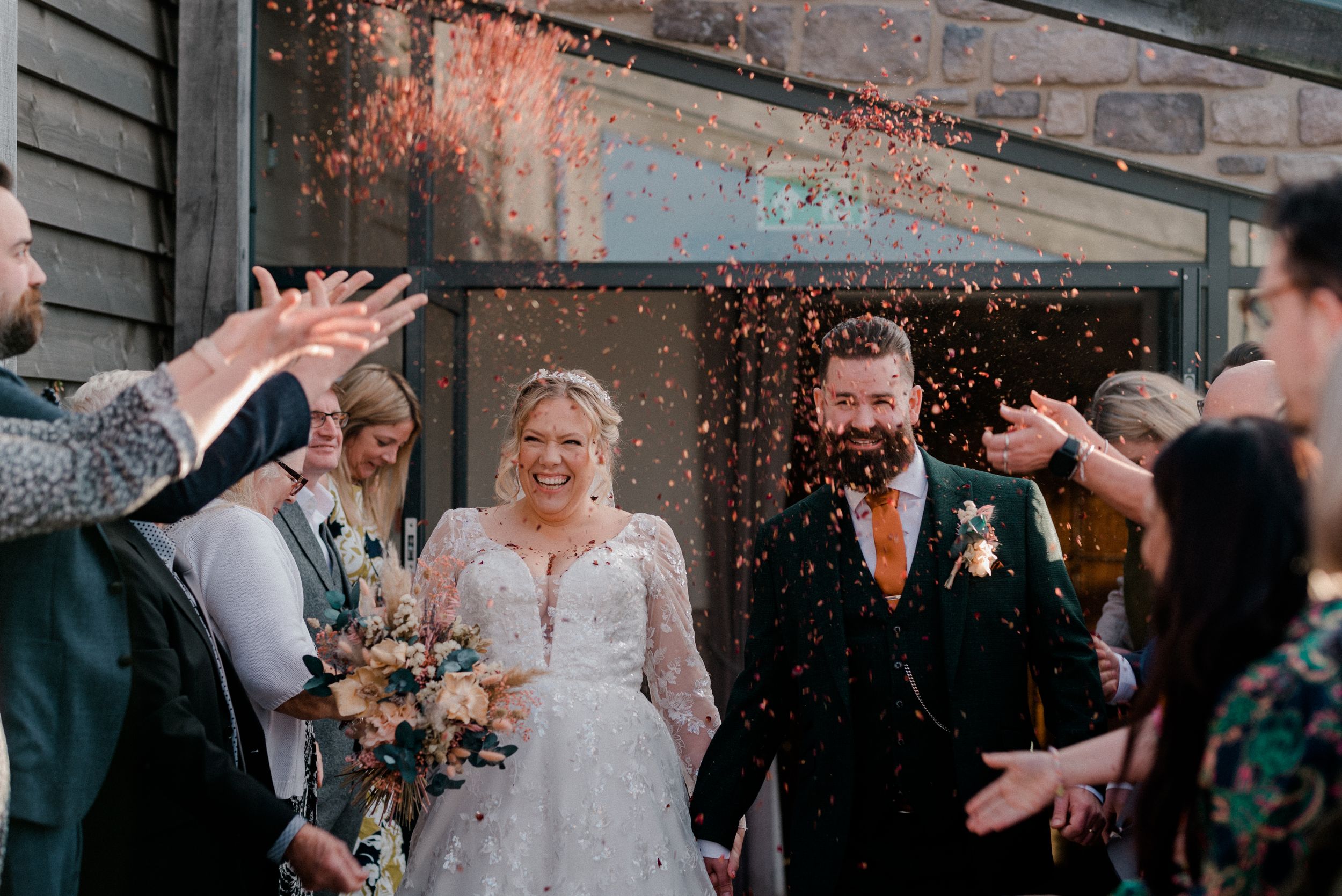 Wedding guests shower the newlyweds with confetti outside the venue.