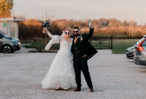 A pair celebrating at their wedding in a car park at sunset, throwing their arms up joyfully.