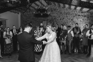 Wedding couple dancing together in a rustic venue while guests watch from the sidelines.