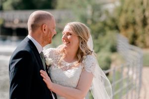 A joyful couple in wedding attire share a candid laughing moment together outdoors in natural lighting.