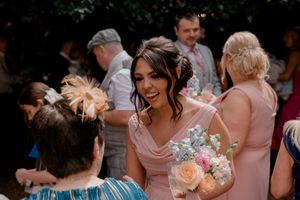 Bridesmaid in pink dress holding bouquet of peach roses during wedding reception.